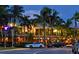 Lively building exterior at twilight with palm trees, outdoor dining, streetlights and parked cars, welcoming ambiance at 800 S Blvd Of Presidents # 12, Sarasota, FL 34236