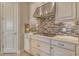 Close-up of the kitchen featuring white cabinets, a stainless steel range hood, and a stylish mosaic tile backsplash at 4020 Cascina Way, Sarasota, FL 34238