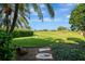 Manicured backyard showcasing lush green grass, mature trees, manicured hedges, and a glimpse of the screened-in pool area at 124 Ventana Way, Venice, FL 34292