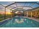 A screened in pool with integrated spa, waterfall feature, sun loungers, and an outdoor kitchen under a sunset sky at 8261 Grande Shores Dr, Sarasota, FL 34240