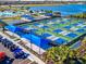 Aerial view of the community's pickleball courts with blue canopies, next to a pool and lake at 10201 Beach Dune Dr, Englewood, FL 34223