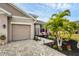 Close-up of a two-car garage, brick paved driveway, and landscaped entrance with palm trees and colorful flowers at 6428 Devesta Loop, Palmetto, FL 34221