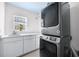 Well-lit laundry room with modern stacked washer/dryer, white cabinetry, and sink beneath a window at 1746 Stapleton St, Sarasota, FL 34239