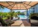 Covered outdoor deck featuring seating, lush landscaping, and view to the beautiful backyard pool at 7453 Featherstone Blvd, Sarasota, FL 34238