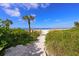 A sandy path leads to a beautiful beach, framed by lush greenery and palm trees at 147 Whispering Sands Dr # V29, Sarasota, FL 34242