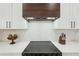 Close up of a modern cooktop featuring a sleek wooden vent hood and white tile backsplash at 3598 Trinity St, North Port, FL 34291