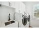 Modern laundry room with white cabinetry, stainless steel sink, and front loading washer and dryer at 3598 Trinity St, North Port, FL 34291