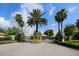Gated community entrance featuring palm trees, colorful plants, and manicured landscaping under a sunny, partly cloudy sky at 4244 Reflections Pkwy, Sarasota, FL 34233