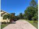 Long brick driveway leading to a yellow house surrounded by lush greenery and a clear blue sky at 15207 17Th E Ave, Bradenton, FL 34212