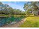 Lush pond view with clear blue water, mature landscaping, and walking path at 28 Tall Trees Ct, Sarasota, FL 34232