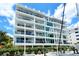 Modern white condo exterior with glass balconies, lush landscaping, and waterfront views at 650 Golden Gate Pt # 403, Sarasota, FL 34236