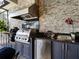 Outdoor kitchen with stainless steel grill, charcoal grill, granite countertop, stainless hood, and a stone backsplash at 8271 Redonda Loop, Lakewood Ranch, FL 34202