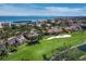Aerial view of the tan-roofed house surrounded by a lush green golf course, lake and ocean with city views at 2065 Harbour Links Dr # 5, Longboat Key, FL 34228