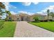 A stunning single-story home shows off an inviting paver driveway leading up to its light stucco exterior and lush landscaping at 9641 Carnoustie Pl, Bradenton, FL 34211