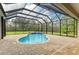 Enclosed pool area featuring brick paver flooring, screened enclosure, waterfall feature, and tropical landscaping at 14538 17Th E Ave, Bradenton, FL 34212