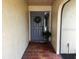 Inviting entryway with brick flooring and a gray front door adorned with a wreath and green plants at 1842 Country Meadows Ct, Sarasota, FL 34235