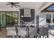The outdoor kitchen has a bar, chairs, stainless appliances, and a view of the pool table inside at 19424 Ganton Ave, Lakewood Ranch, FL 34202