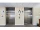 Two stainless steel elevators in a condo building, featuring call buttons and signage at 3730 Cadbury Cir # 414, Venice, FL 34293