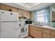 Bright kitchen featuring white appliances, wood cabinets, and a window with blue curtains at 2907 51St W Ave, Bradenton, FL 34205