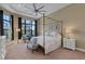 A bedroom with a four-poster bed, neutral walls, a tray ceiling with fan and a view of the yard at 8901 Artisan Way, Sarasota, FL 34240