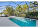 A beautiful in-ground pool is the focal point of this screened enclosure, surrounded by lush landscaping and a sunny sky at 11603 Gramercy Park Ave, Bradenton, FL 34211