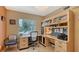 Bright home office featuring custom built-in shelving, a desk, and a window with a view of the backyard pool at 940 Siesta Key Pl, Sarasota, FL 34242