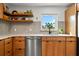 Beautiful kitchen with wooden cabinets, stainless steel dishwasher, floating shelves, sink, and tiled backsplash at 1239 Pinebrook Way, Venice, FL 34285