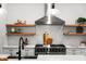 Close-up of a kitchen featuring stainless steel vent hood, gas range, floating shelves, and quartz countertops at 597 Buttonwood Dr, Longboat Key, FL 34228
