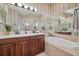 Well-lit bathroom featuring double sinks, a soaking tub, wood cabinets and elegant lighting fixtures at 5141 Lansdowne Way, Palmetto, FL 34221