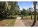 View of a tree lined gravel entry with a brick path, black fence, mature trees and lush, green lawn at 4920 Kestral Park Cir # 11, Sarasota, FL 34231