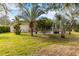 Lush backyard with green grass and tropical trees, and a glimpse of the screened in pool at 10306 Palmbrooke Ter, Bradenton, FL 34202