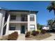 Two-story condo building featuring a front door, balcony, and lush landscaping against a blue sky at 4440 47Th W Ave # 204, Bradenton, FL 34210