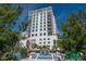 A modern white building with glass balconies, set against a blue sky and framed by green trees and a public square at 512 Laurel Park Dr, Sarasota, FL 34236