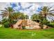 Landscaped entrance to River Strand featuring a rock waterfall and lush tropical foliage beneath a blue, partly cloudy sky at 7112 Marsh View Ter, Bradenton, FL 34212