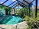 Screened-in pool area with a waterfall feature, lush landscaping, and views of surrounding homes at 1428 Pine Island Ct, Punta Gorda, FL 33950