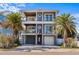 Three-story coastal home featuring dual balconies, a red front door, and tropical palm trees at 108 Magnolia Ave, Anna Maria, FL 34216