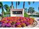 Fiesta Harbor entrance sign with colorful flowers, tropical foliage, and palm trees under a sunny blue sky at 1250 N Portofino Dr # 408Mar, Sarasota, FL 34242