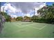Brightly lit tennis court with manicured green surface, surrounded by mature trees and lush landscaping on a sunny day at 4330 47Th W Ave # 104, Bradenton, FL 34210
