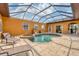Aerial view of a screened-in pool with hot tub, patio furniture, and colorful orange exterior walls at 10494 Atenia St, Port Charlotte, FL 33981