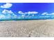 Expansive view of sandy beach and ocean waves beneath a bright blue sky dotted with fluffy white clouds at 1465 Gulf Of Mexico Dr # 104, Longboat Key, FL 34228
