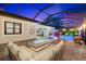A luxurious screened-in pool area with a modern fire pit, outdoor kitchen and plenty of seating at night at 1805 7Th St E, Palmetto, FL 34221