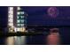 Night view of a modern waterfront building with a festive fireworks display and lights reflecting on the water at 5655 Downham Mdws, Sarasota, FL 34235