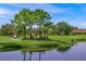 Scenic golf course view with players and a calm lake surrounded by lush trees and greenery at 7108 Callander Cv, Lakewood Ranch, FL 34202