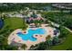 Aerial view of a community pool featuring a unique shape, lounge chairs, palm trees, and a clubhouse in a lush, landscaped setting at 7108 Callander Cv, Lakewood Ranch, FL 34202