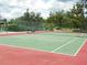 Well-maintained outdoor tennis court with red and green surface, surrounded by greenery and a fence at 6042 Red Maple Rd # 1001, Bradenton, FL 34210
