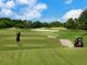 Scenic golf course with a golfer teeing off amidst rolling greens, sand traps, and a passing golf cart at 6316 Walton Heath Pl, University Park, FL 34201