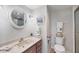 Bathroom with a round mirror, vanity, toilet, framed artwork, and tiled shower area, creating a functional and inviting space at 101 Benjamin Franklin Dr # 63, Sarasota, FL 34236