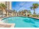 Beautiful building featuring a luxury pool, lounge chairs and tables, and swaying palm trees under a sunny sky at 1300 Benjamin Franklin Dr # 304, Sarasota, FL 34236