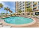 Beautiful building featuring a luxury pool, lounge chairs and tables, and swaying palm trees under a sunny sky at 1300 Benjamin Franklin Dr # 304, Sarasota, FL 34236