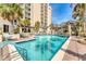 Beautiful building featuring a luxury pool, lounge chairs and tables, and swaying palm trees under a sunny sky at 1300 Benjamin Franklin Dr # 304, Sarasota, FL 34236